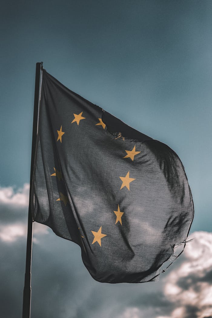 about-01 European Union flag gently waving on a flagpole against a cloudy sky, symbolizing unity and patriotism.